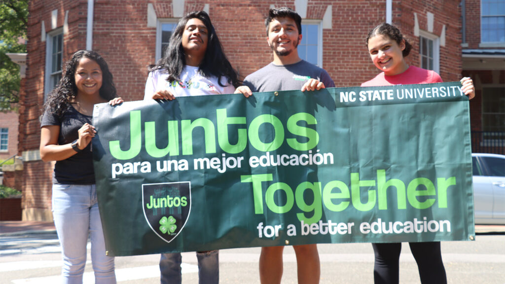 Rios and three other people stand outside and hold a large green banner that reads "Together for a better education."