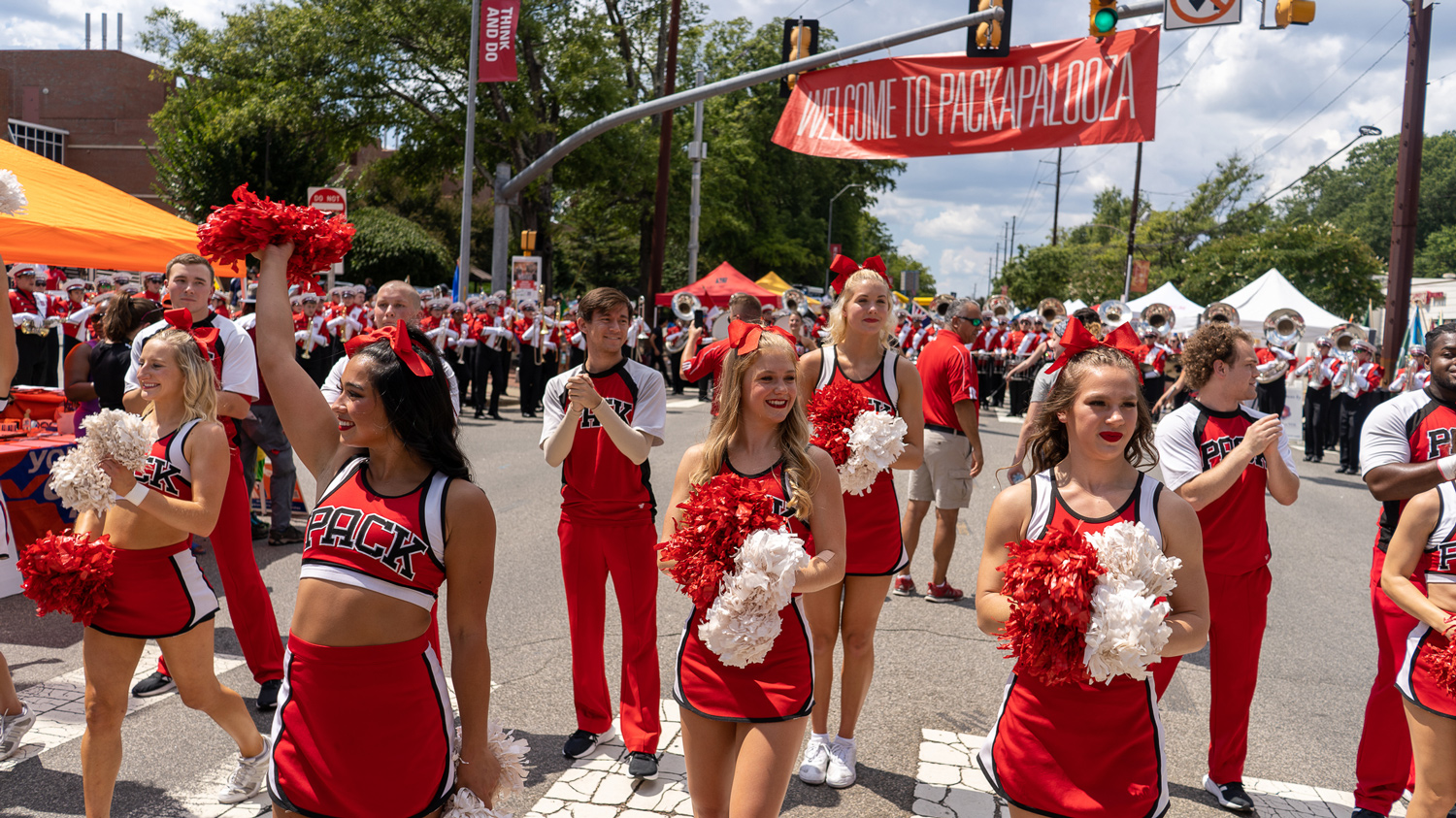 Cheerleaders with the marching band in the background under the Packapalooza street banner on Hillsborough Street.