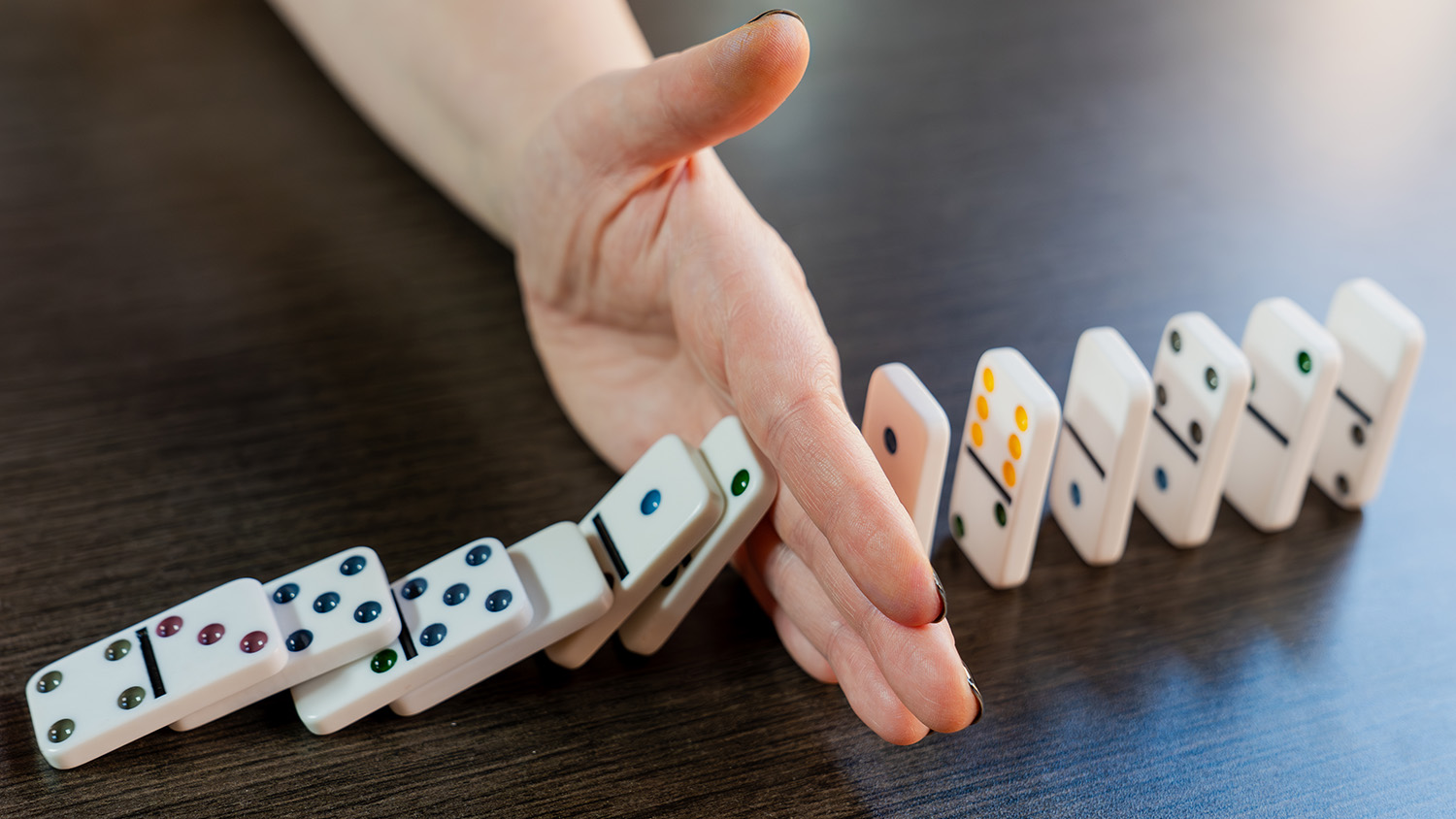 A hand interrupts a line of falling dominoes.
