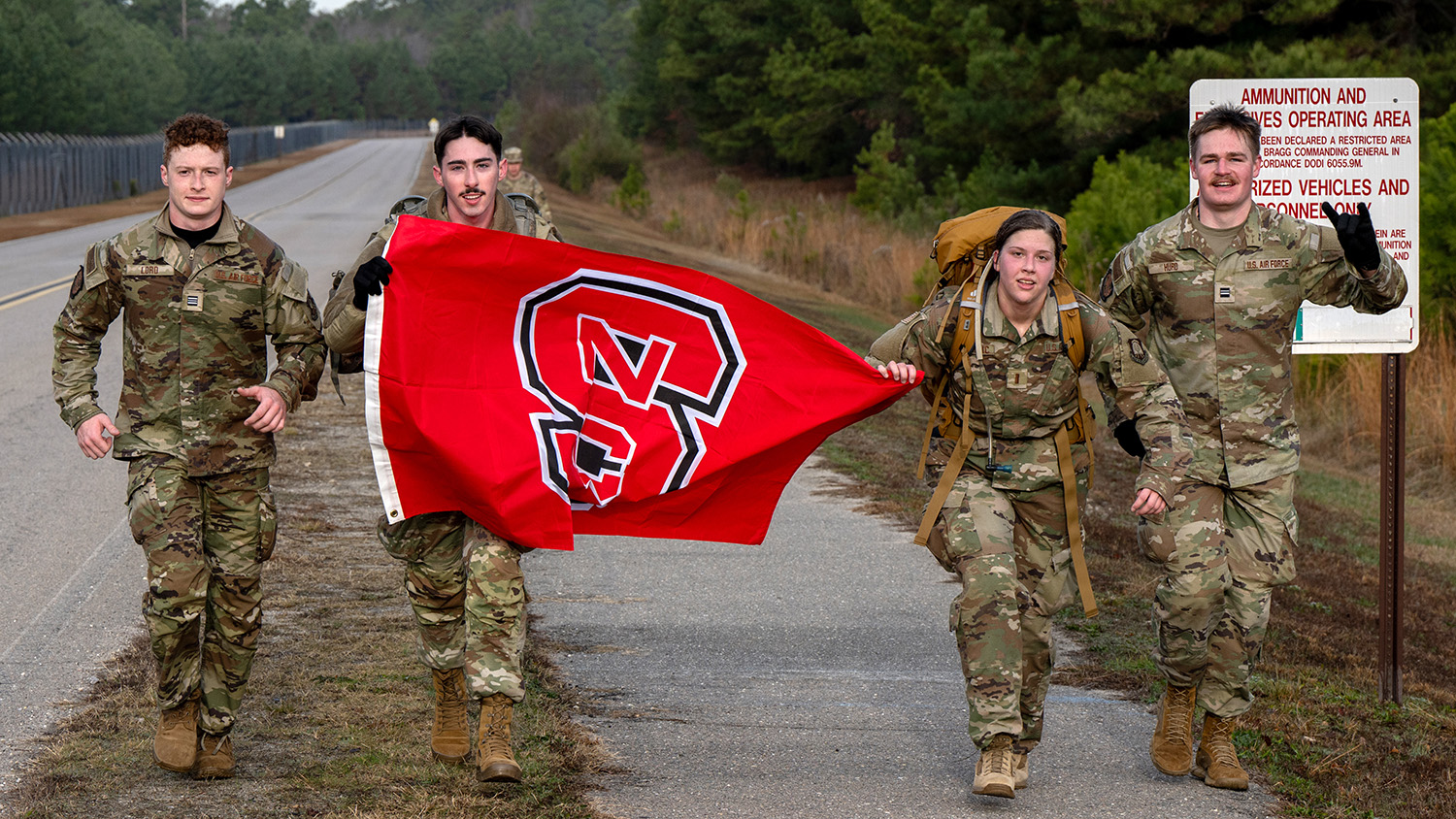 From left, NC State Air Force ROTC Cadets Jace Lord, Dillon Curtis, Amina Becirovic and Josh Hurd march with an NC State flag during the German Armed Forces Proficiency Badge testing at Fort Liberty.