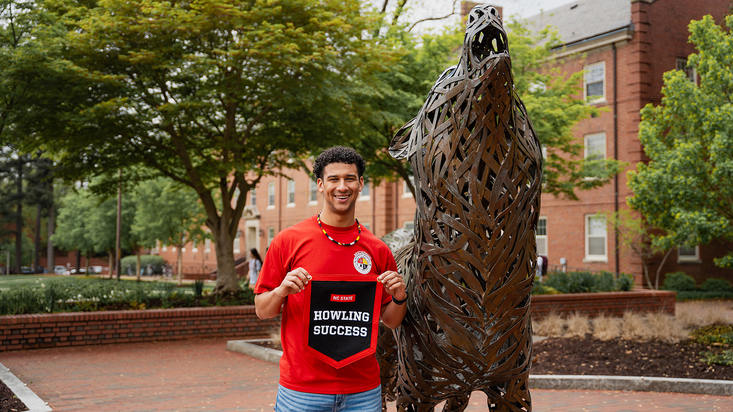 Nathan Campbell shows off his Howling Success banner in front of the Wolf Plaza statues.