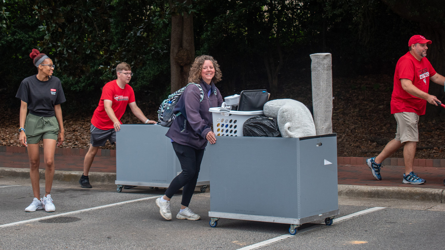 Students and parents with carts full of student belongings walking through the parking lot to their residence hall to move into their space.