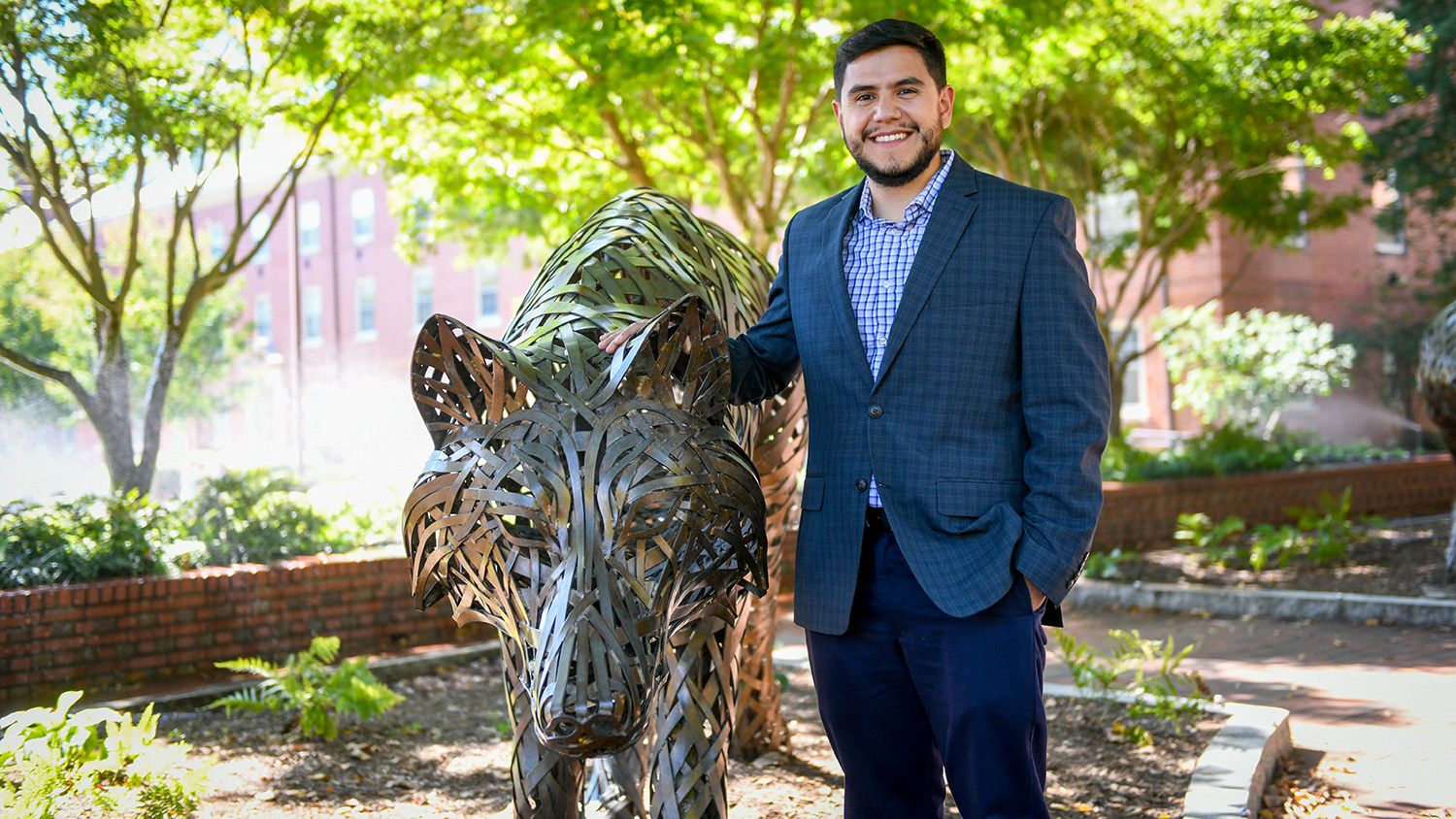 Julio Terán, an academic adviser and lecturer in the Engineering first-year program, with a Wolf Plaza statue.