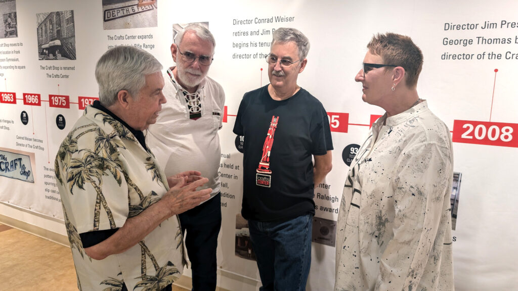 Current and former Crafts Center directors chat in front of a timeline celebrating the center's history. 