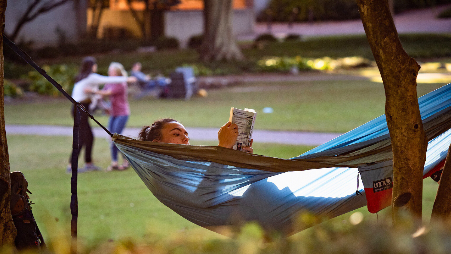 Student reading a book in a hammock on campus