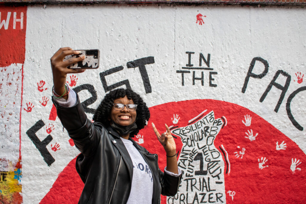 A First in the Pack Participant takes a picture in front of the program's mural.