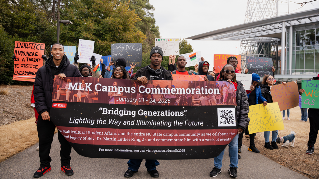Students march forward with an MLK Campus Commemoration banner.