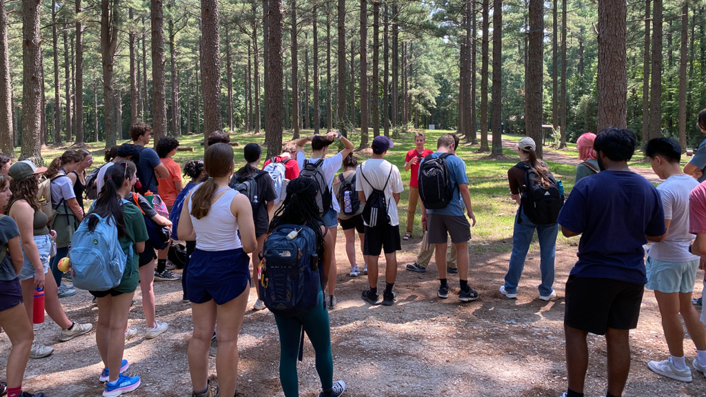 Fall 2024 ENV 101-005H Honors students gather around Dr. Robert Scheller, Associate Dean for Research in the College of Natural Resources, as he discusses the forestry industry's attempts to adapt to impacts due to climate change out at NC State-owned Carl Alwin Schenck Memorial Forest.