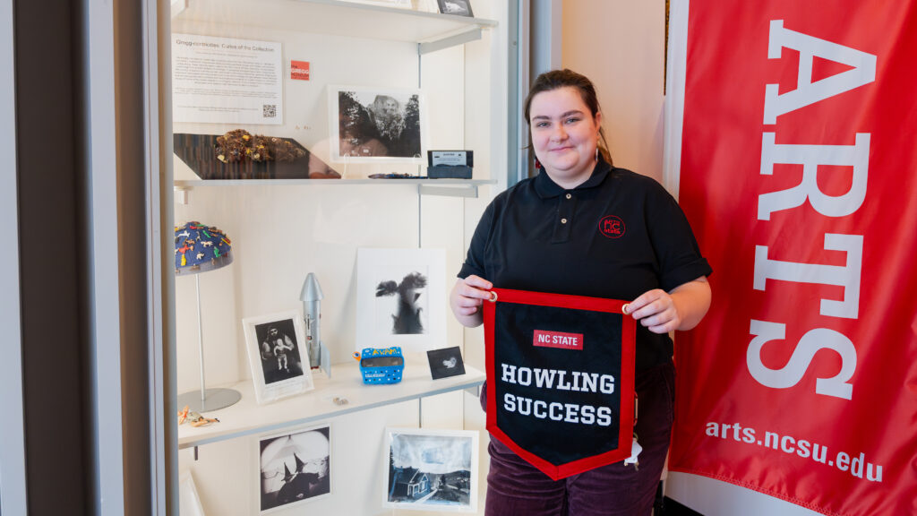 Bee Mangine displays their Howling Success banner in front of an Arts NC State display.
